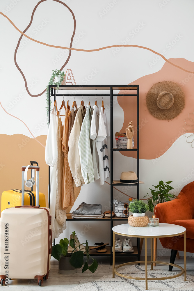 Shelving unit with clothes and accessories in interior of stylish room