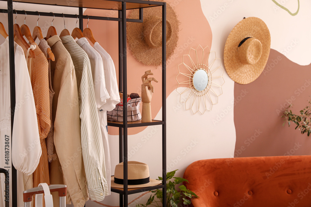 Shelving unit with clothes and accessories near color wall in room