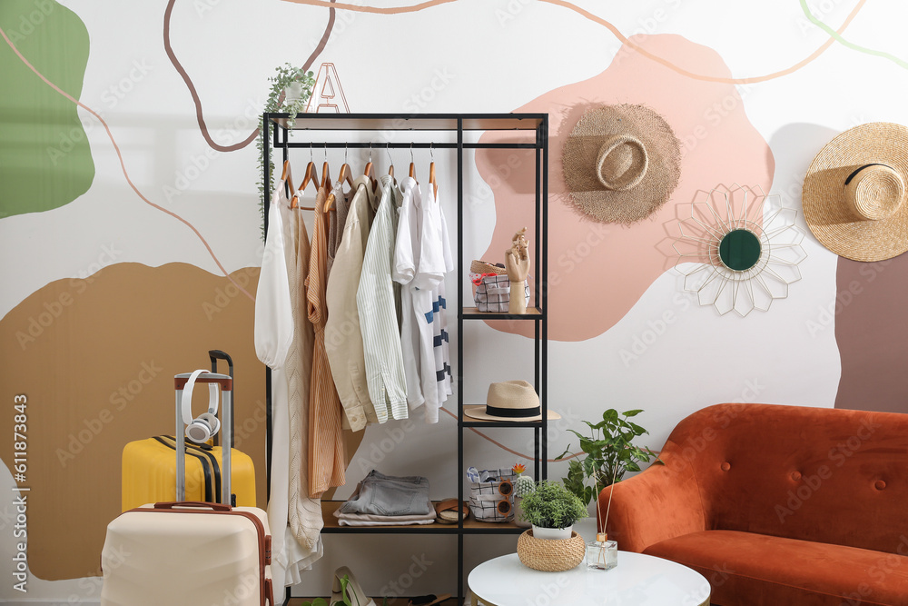 Shelving unit with clothes and accessories in interior of stylish room