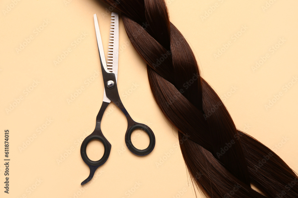 Braided hair strand with scissors on beige background