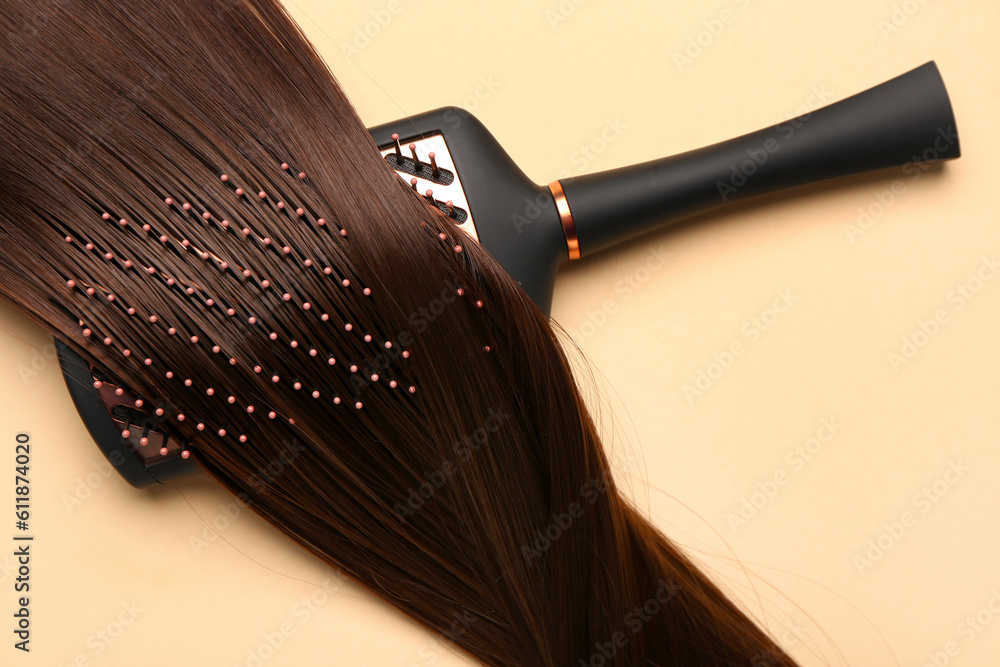 Hair strand with brush on beige background, closeup