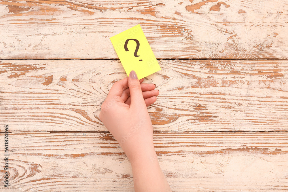 Female hand and sticky note with question mark on white wooden background