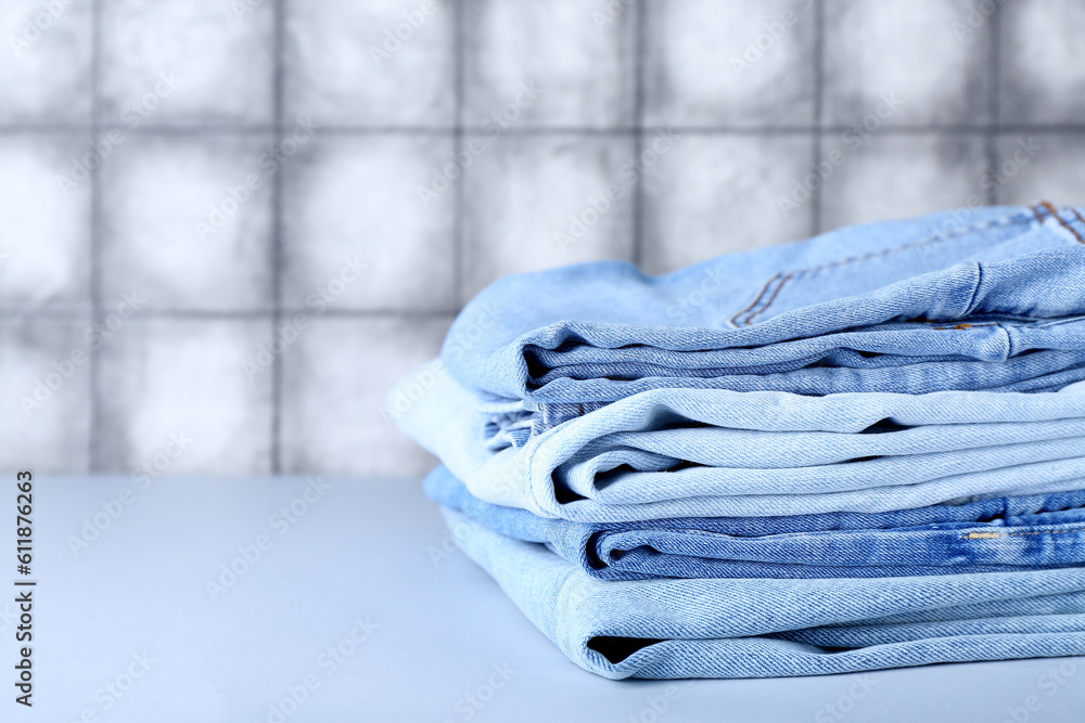 Stack of jeans on table near grey tile wall