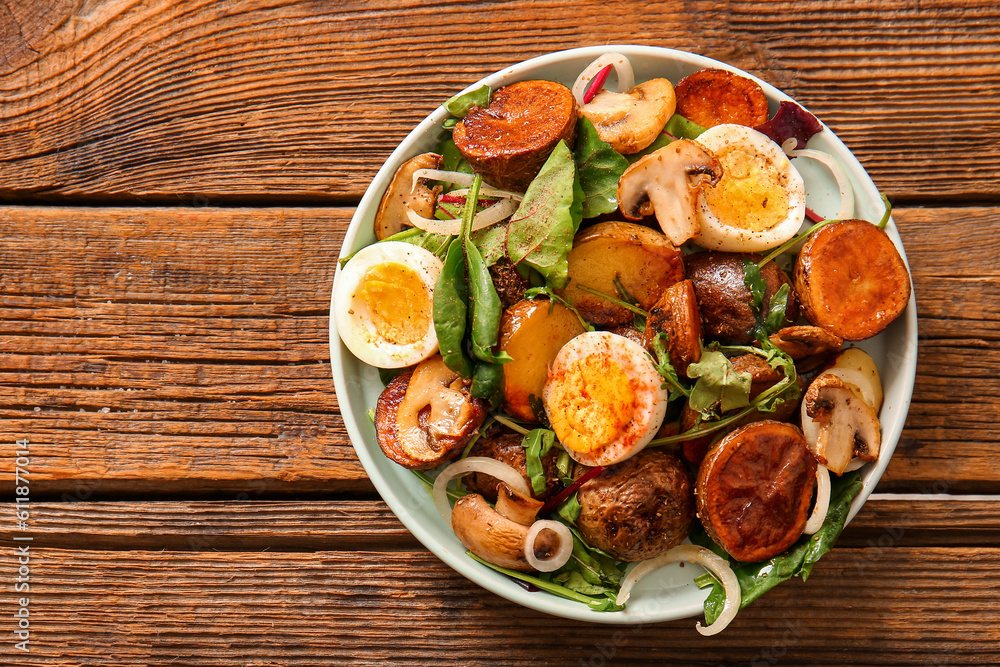 Plate of tasty potato salad with eggs and mushrooms on wooden background, top view