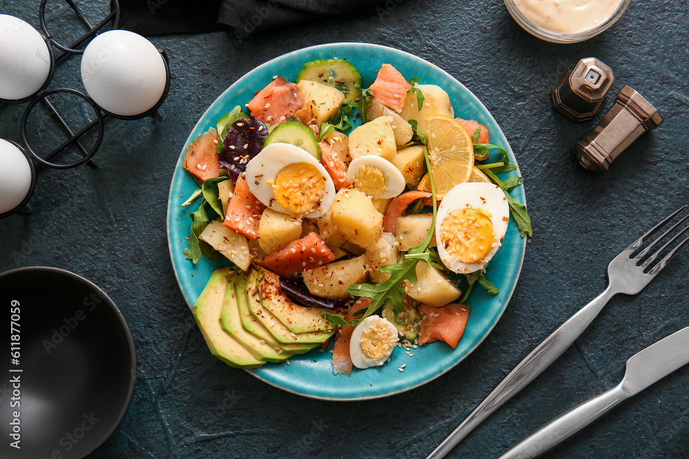 Plate of tasty potato salad with eggs and avocado on dark background, top view