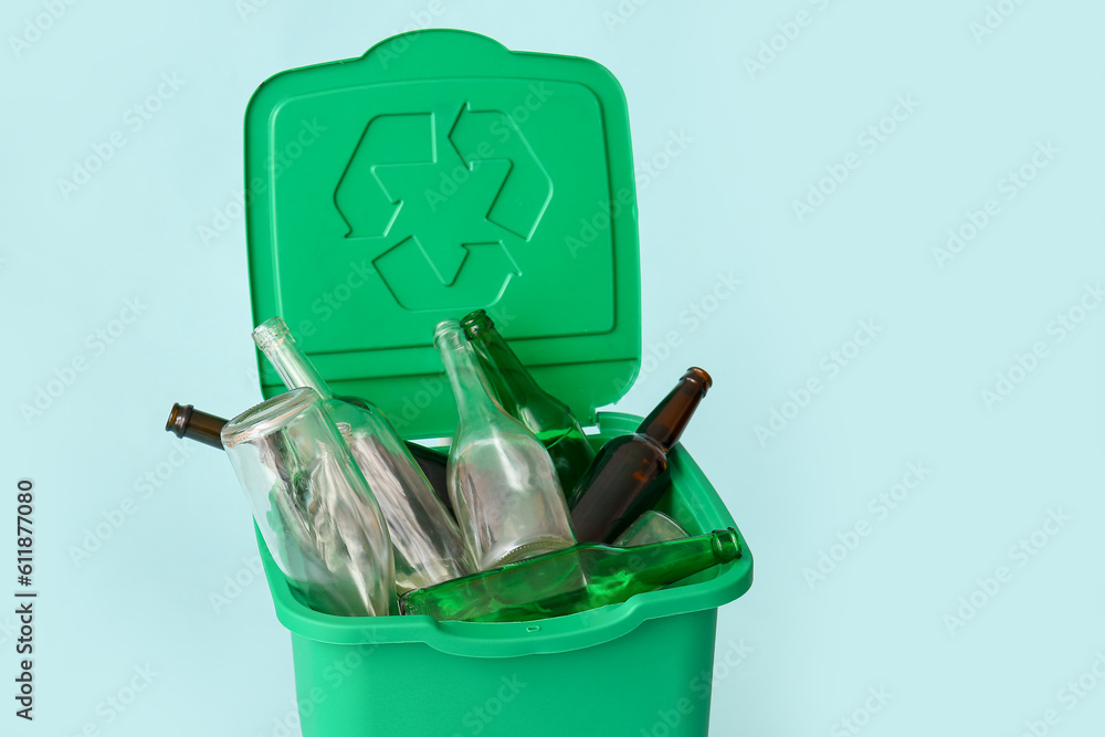 Container for garbage with glass bottles on light blue background. Recycling concept