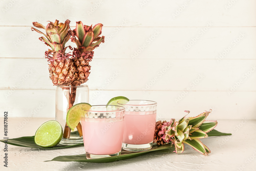 Glasses of cocktail with lime, baby pineapples and palm leaves on white table