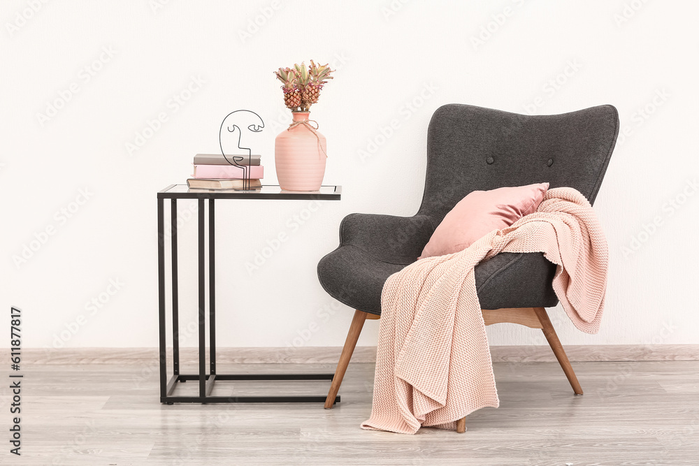 Vase with baby pineapples, books on table and armchair in living room