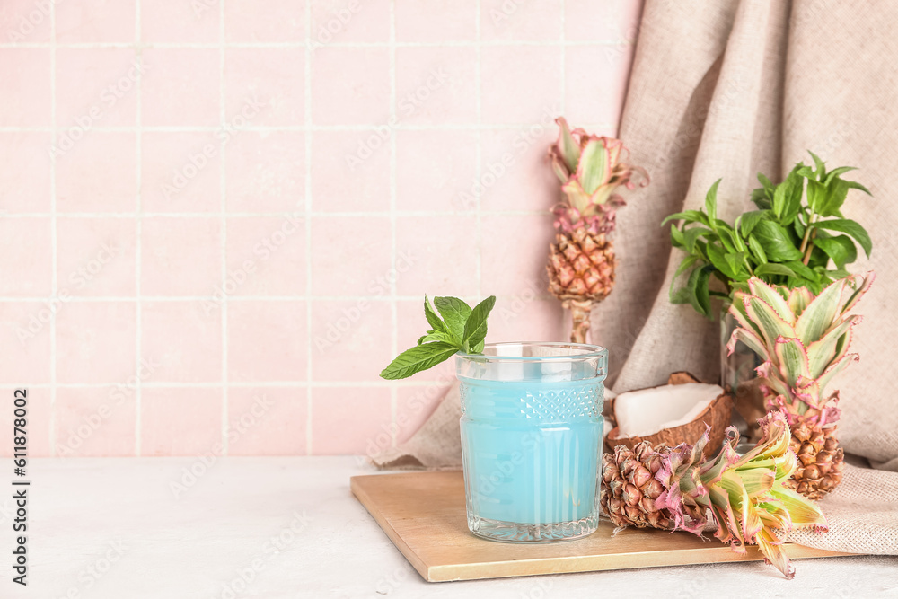 Glass of cocktail with mini pineapples on table near pink tile wall