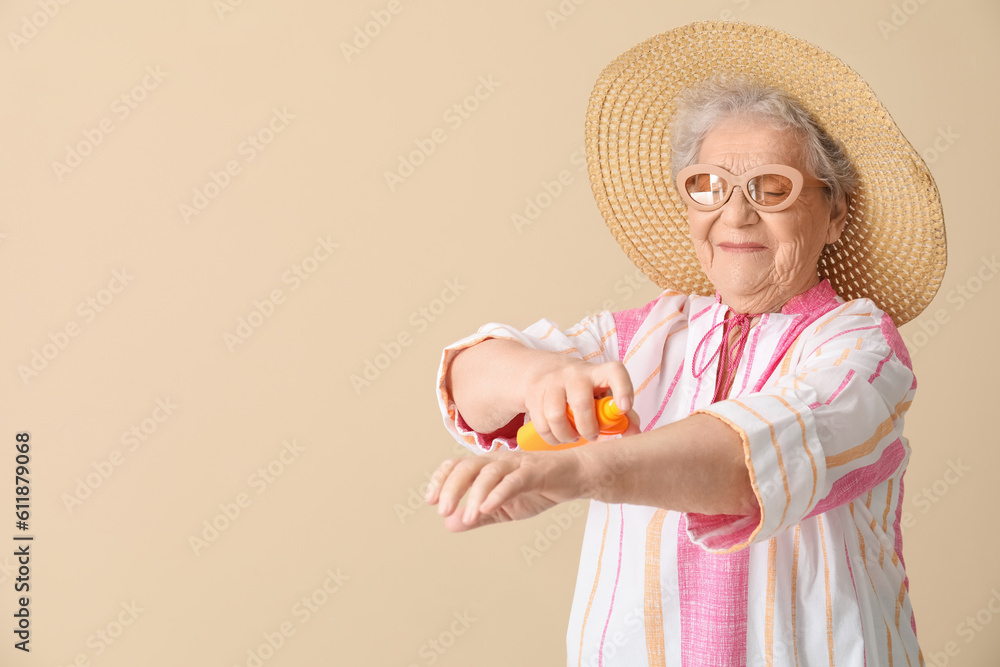 Senior woman applying sunscreen cream on beige background