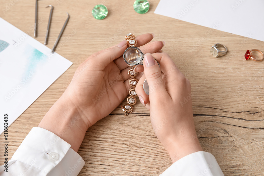 Female jeweler examining bracelet on wooden table, closeup