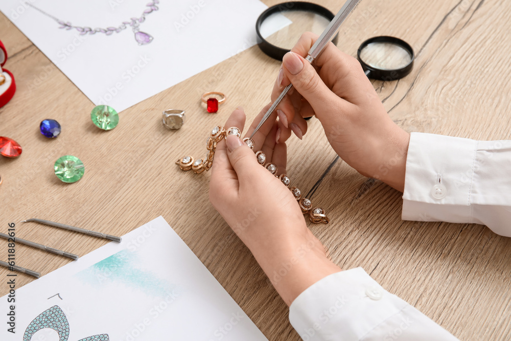 Female jeweler making bracelet on wooden table, closeup