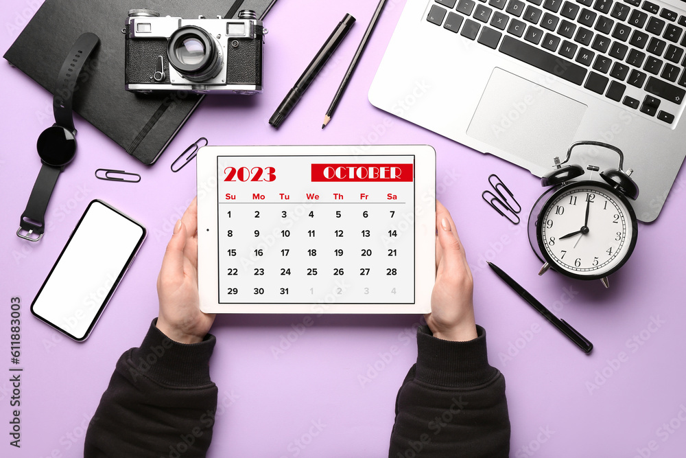 Woman holding tablet computer with calendar near different gadgets on lilac background