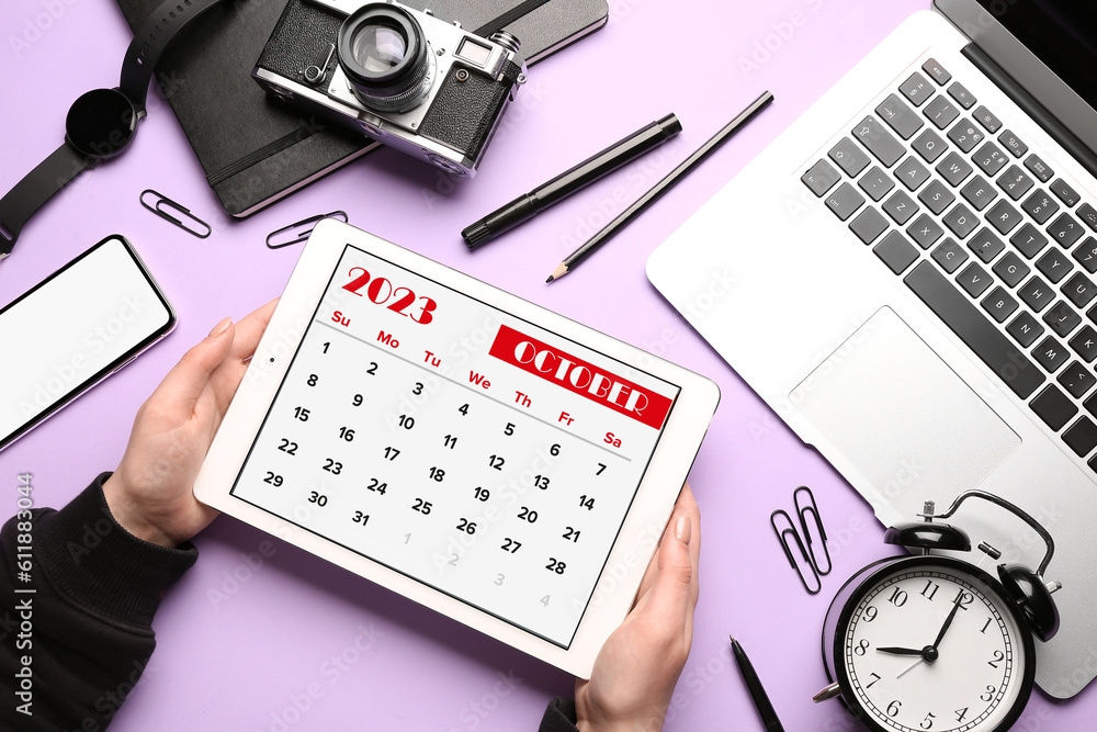 Woman holding tablet computer with calendar near different gadgets on lilac background