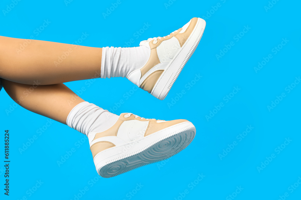 Female legs in stylish sneakers on color background, closeup