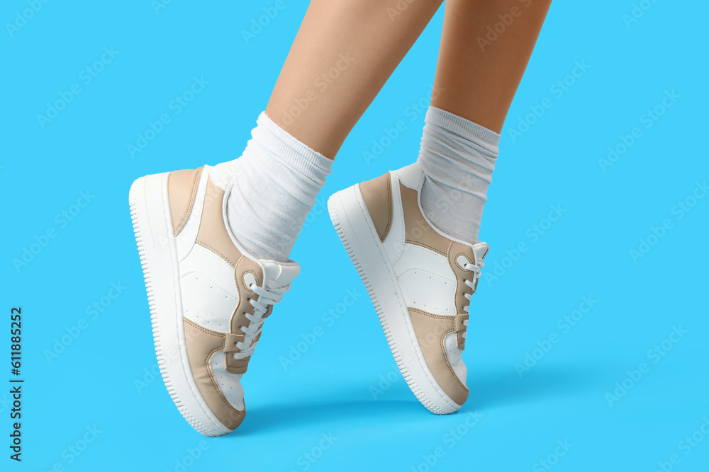 Female legs in stylish sneakers on color background, closeup