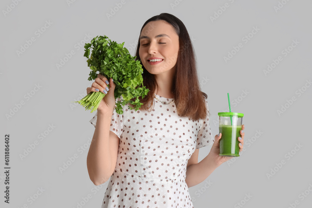 Young woman with glass of vegetable juice and parsley on grey background