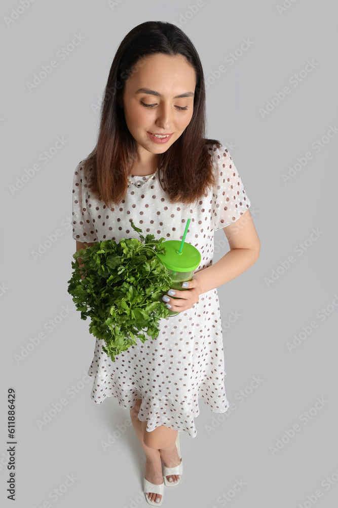 Young woman with glass of vegetable juice and parsley on grey background