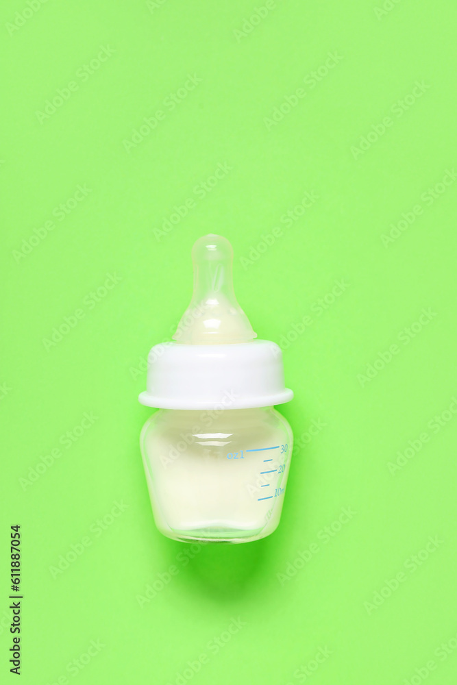 Bottle of milk for baby and accessories on pale green background