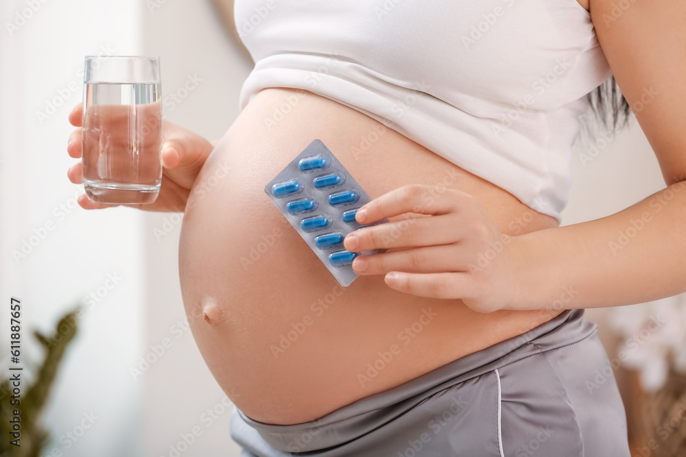 Pregnant woman with Folic Acid pills and glass of water at home, closeup