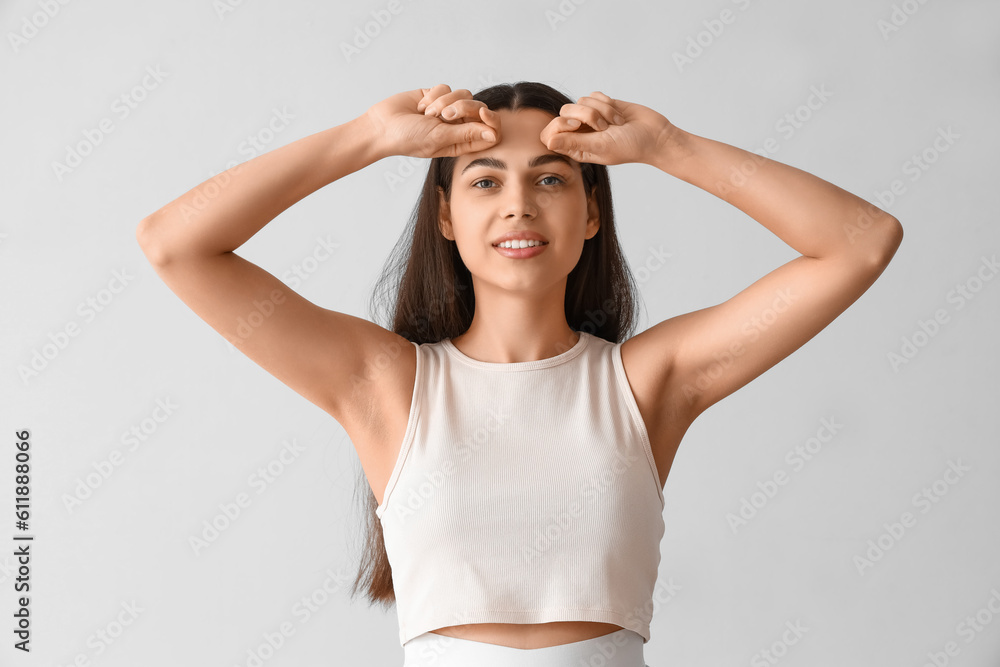 Young woman doing face building exercise on light background