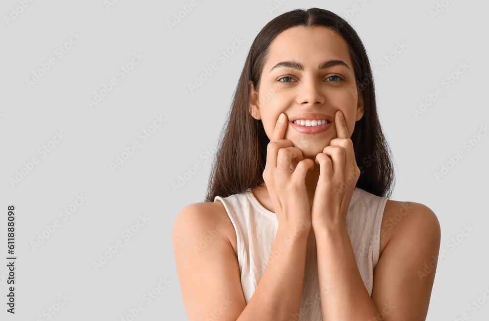 Young woman doing face building exercise on light background, closeup