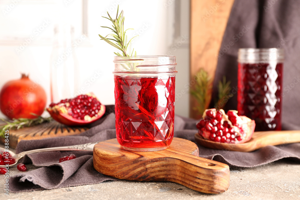 Spoon with fresh pomegranate and glasses of juice on grey table