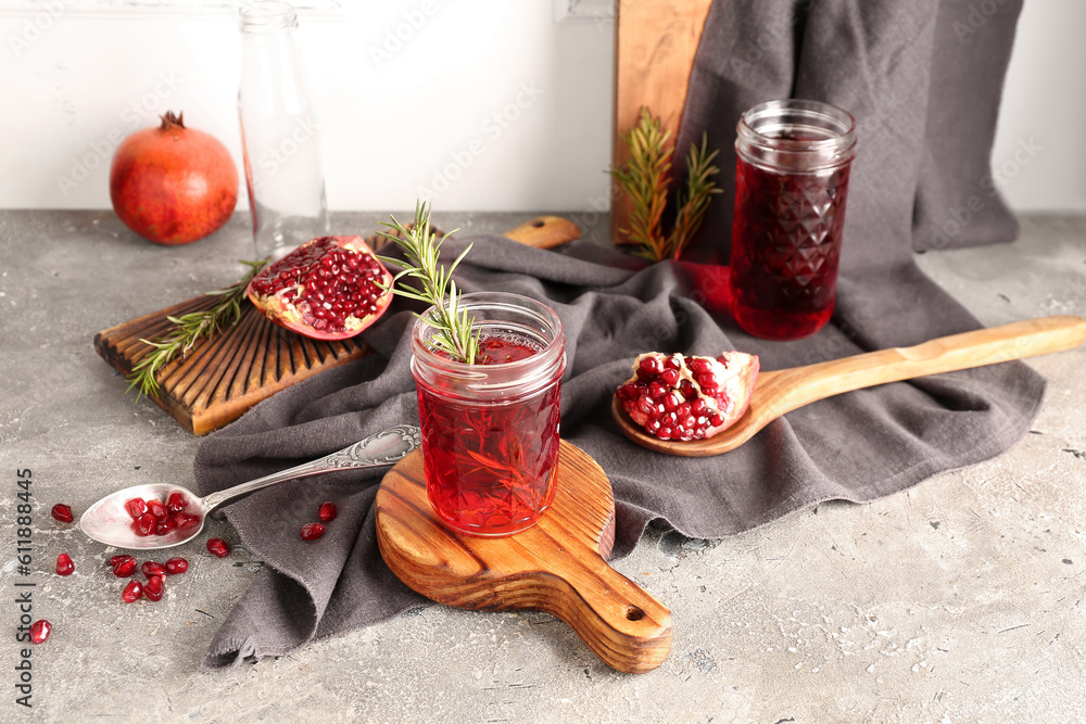 Spoon with fresh pomegranate and glasses of juice on grey table