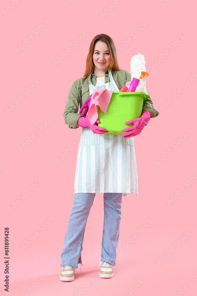 Young woman with cleaning supplies on pink background