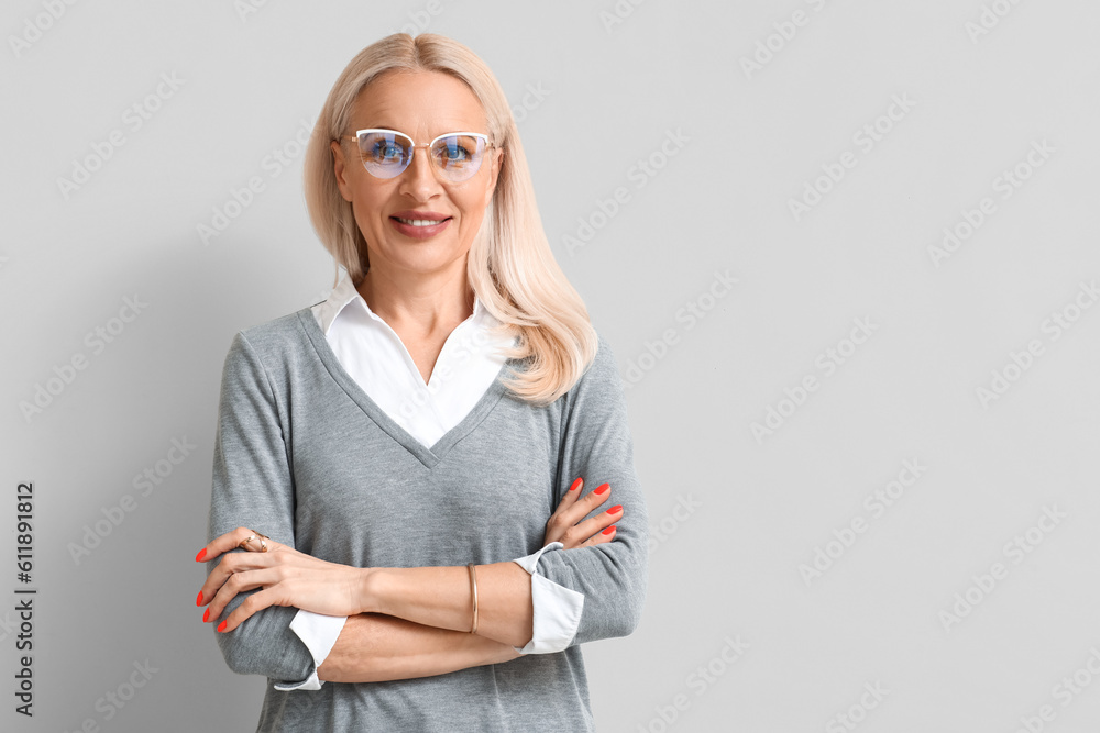 Mature blonde woman in eyeglasses on light background