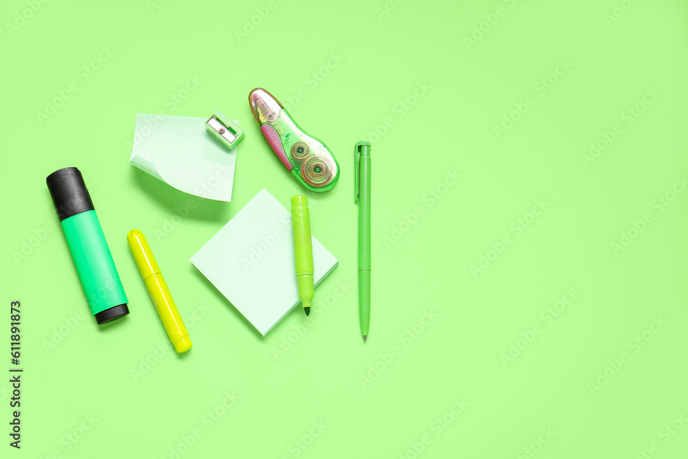 Sticky notes with different stationery supplies on green background