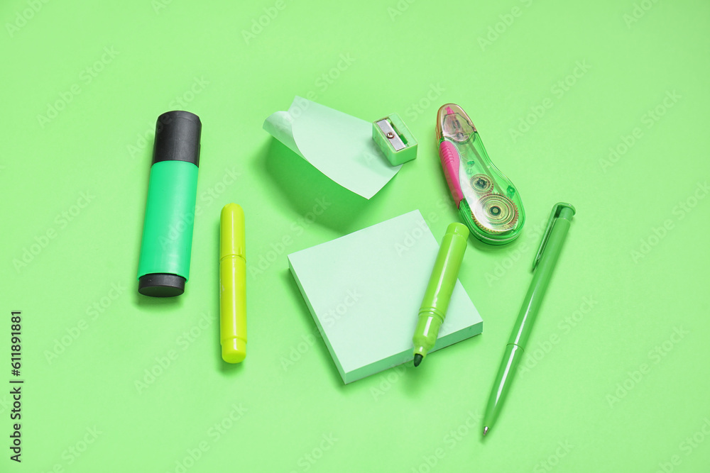 Sticky notes with different stationery supplies on green background