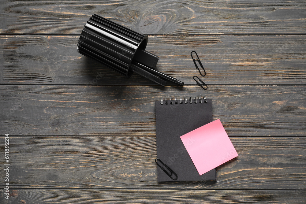 Sticky notes with notebook and pen holder on black wooden background