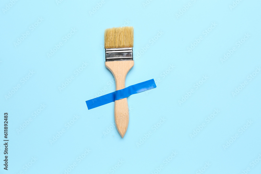 Paint brush with adhesive tape on blue background