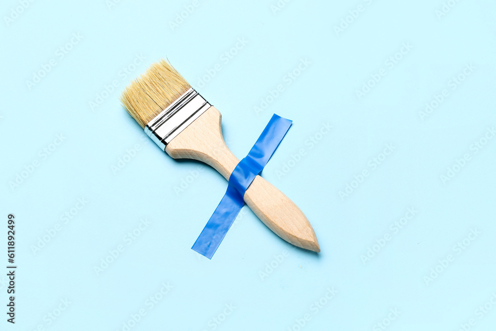 Paint brush with adhesive tape on blue background