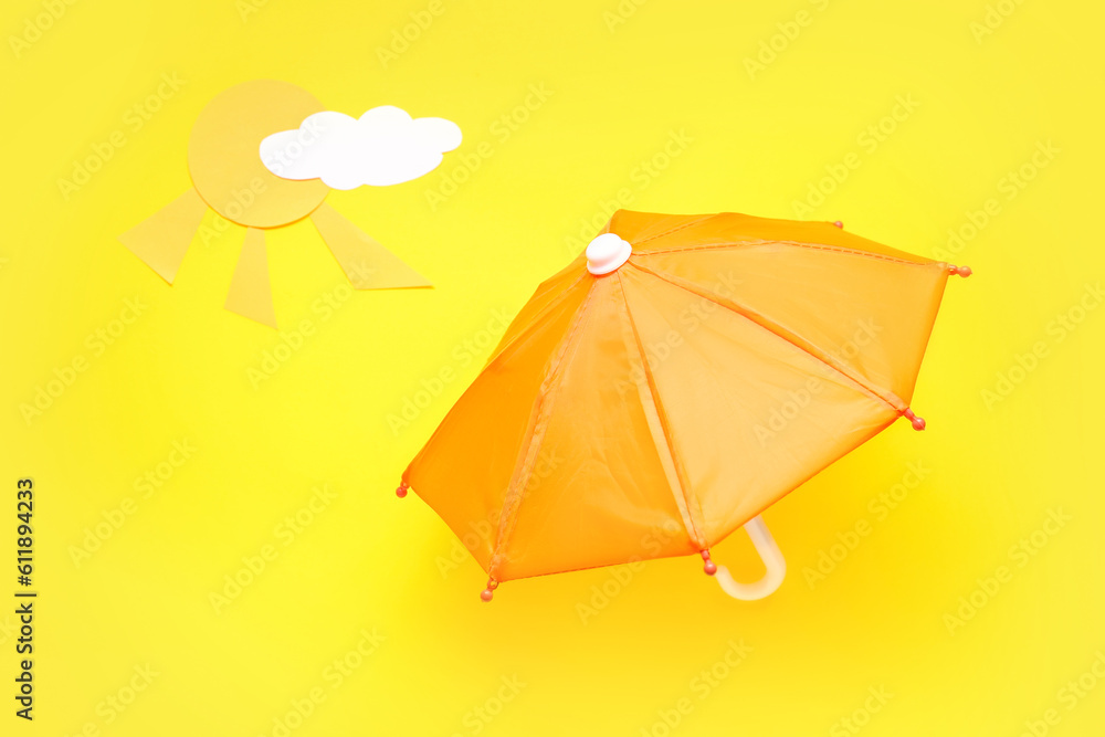 Creative composition with umbrella, paper cloud and sun on yellow background