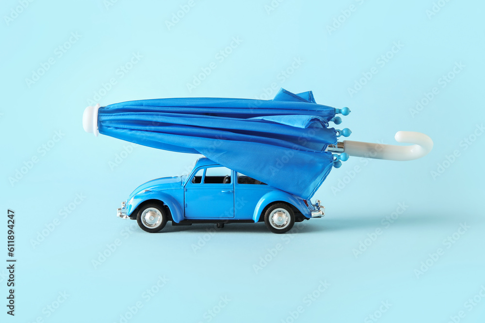 Creative composition with toy car and mini umbrella on blue background. Insurance concept