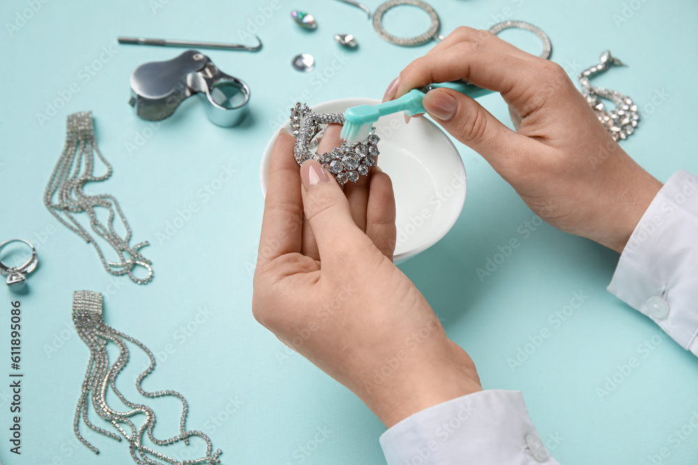 Woman cleaning beautiful earring with toothbrush on blue background, closeup