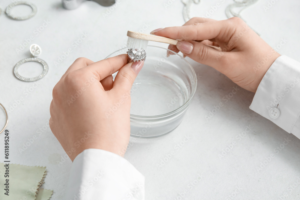 Woman cleaning beautiful ring with toothbrush on light background, closeup