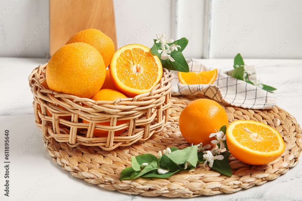 Basket of oranges with blooming branches on white table