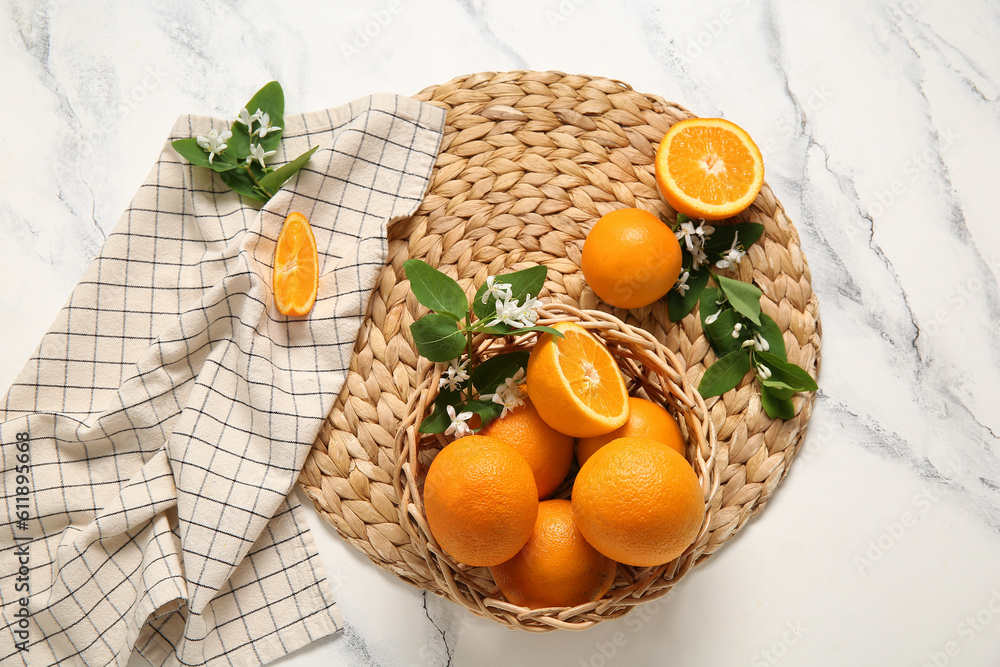 Basket of oranges with blooming branches on white table