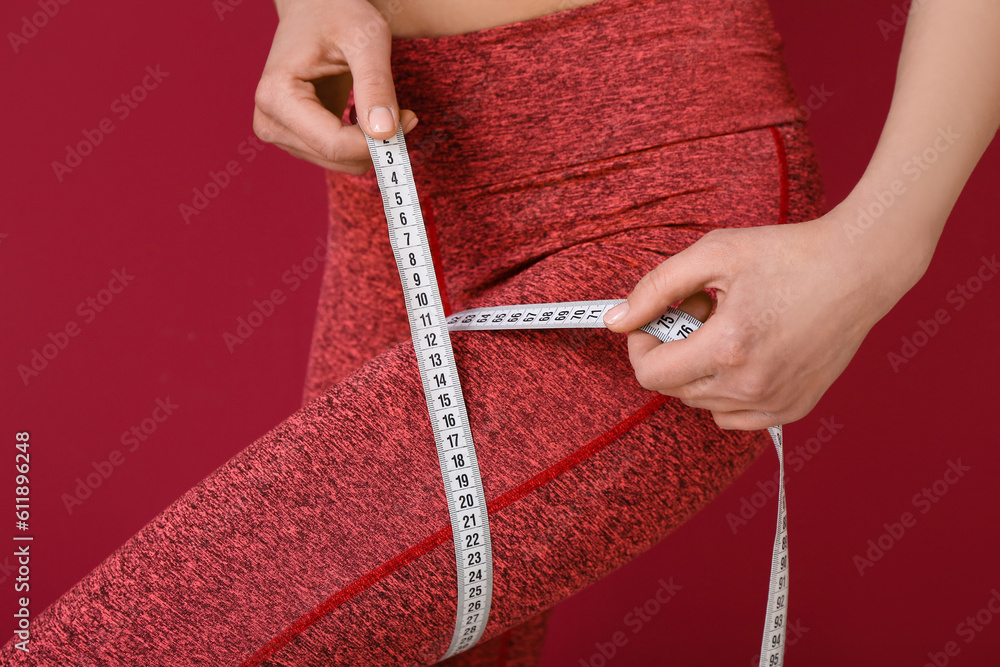 Young woman with measuring tape on burgundy background, closeup. Diet concept