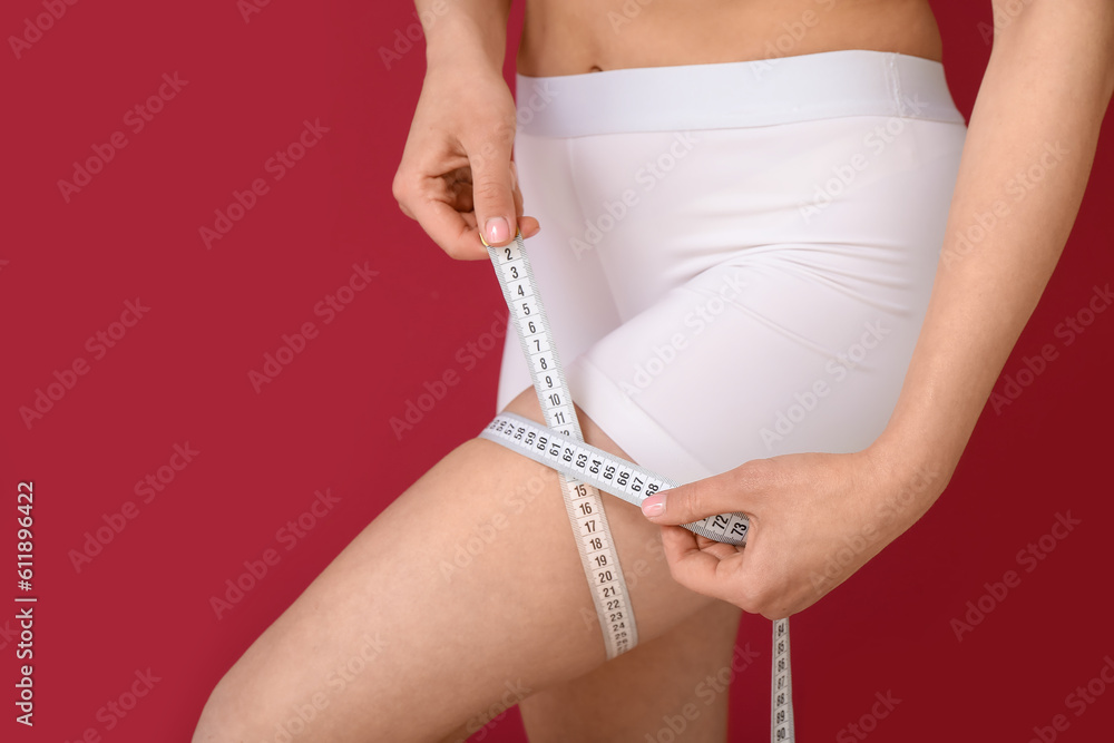 Young woman with measuring tape on burgundy background. Diet concept