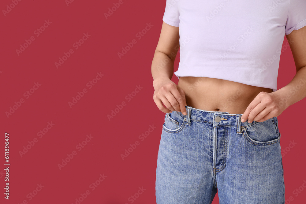 Young woman in loose jeans on burgundy background. Diet concept