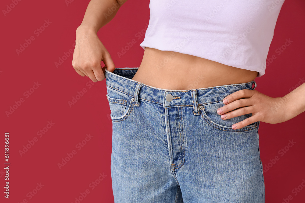 Young woman in loose jeans on burgundy background. Diet concept