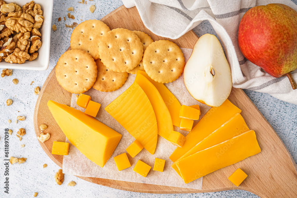 Board with tasty cheddar cheese, pear, crackers and nuts on light background