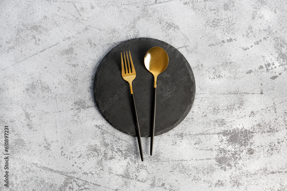 Board with golden spoon and fork on grey background