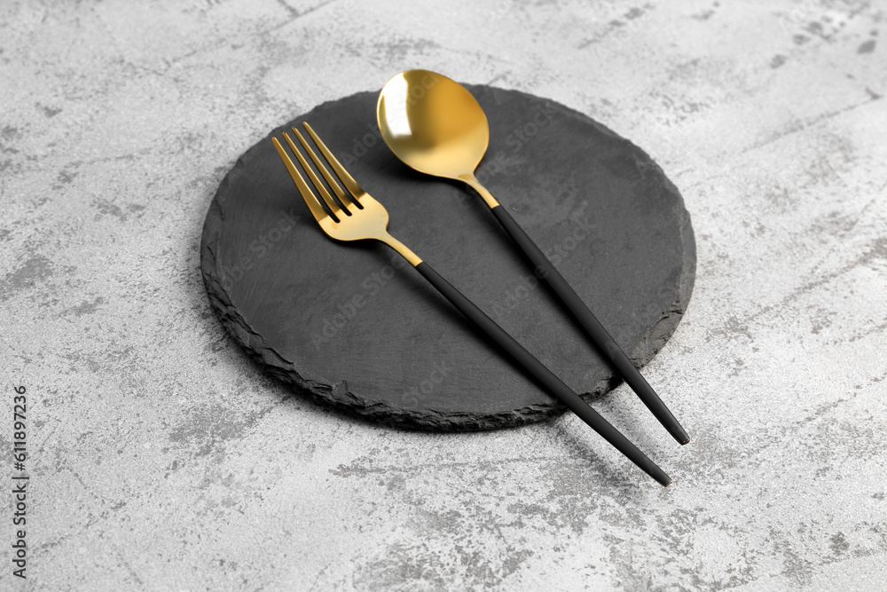 Board with golden spoon and fork on grey background