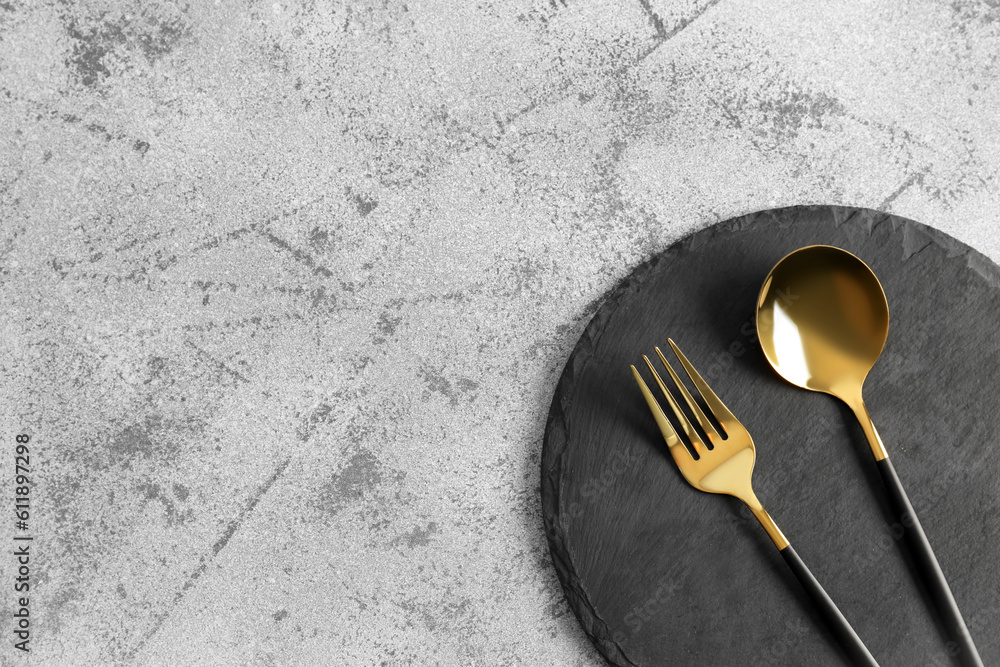 Board with golden spoon and fork on grey background