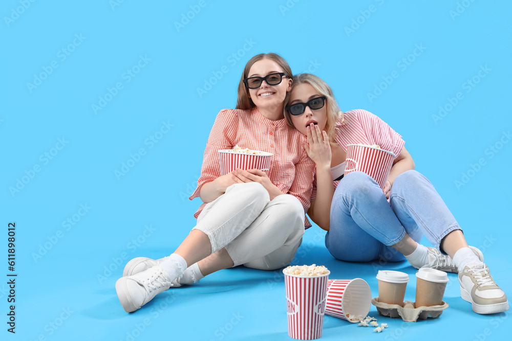 Young sisters in 3D glasses with popcorn on blue background